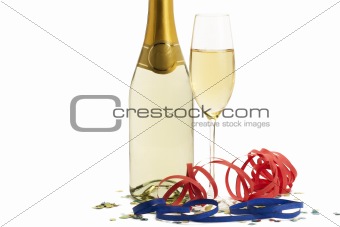 glass of champagne with blow-outs and confetti in front of a champagne bottle