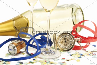 two glasses with champagne, old pocket watch, streamer, cork and confetti in front of a champagne bottle