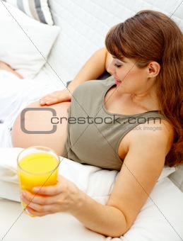 Beautiful pregnant female relaxing on sofa with glass of juice  in hand
