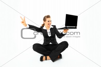 Smiling modern business woman sitting on floor with laptops and showing victory gesture
