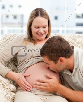 Proud man kissing the belly of his pregnant girlfriend sitting i