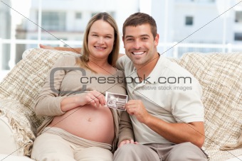 Happy couple showing an echography to the camera both sitting on