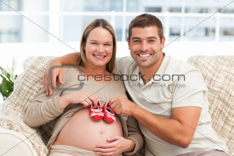 Future parents playing with baby shoes sitting on the sofa