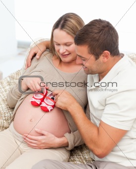Handsome future dad putting baby shoes his wife's belly