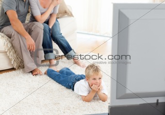 Attentive little boy watching television lying on the floor