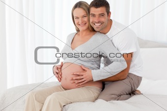 Lovely future parents hugging sitting in the bedroom at home