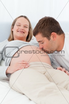 Lovely man kissing the belly of his pregnant wife in the bed
