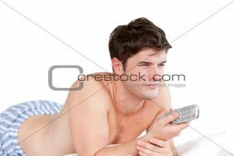 Handsome man holding a remote lying on his bed