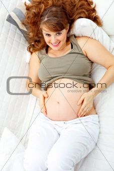 Happy beautiful pregnant woman relaxing on  couch and  holding her belly
