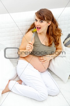 Smiling beautiful pregnant woman sitting on sofa and  eating pickle
