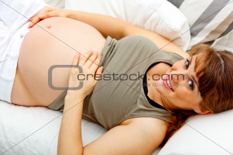 Smiling beautiful pregnant woman relaxing on couch and  holding her belly
