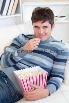 Handsome young man eating popcorn lying on the sofa