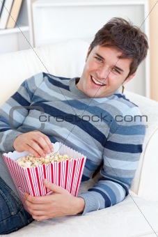 Delighted young man eating popcorn lying on the sofa
