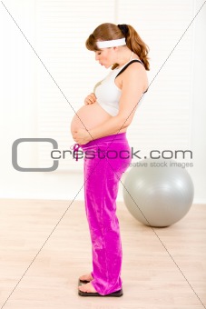 Pregnant woman standing on weight scale and blowing kiss her belly

