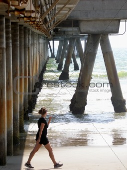 Woman walking on shore under walkway pillars