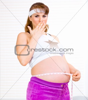 Shocked beautiful pregnant woman measuring her belly
