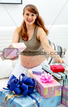 Happy  beautiful pregnant female sitting on sofa with gifts for her unborn baby
