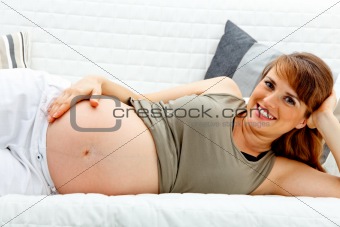 Smiling beautiful pregnant woman relaxing on sofa and  holding her tummy.
