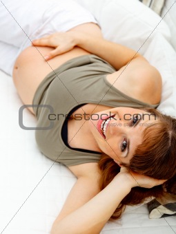 Smiling beautiful pregnant female lying on sofa and  holding her belly.
