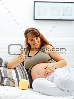 Smiling beautiful pregnant woman knitting for her baby.
