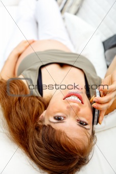 Smiling beautiful pregnant woman relaxing on couch and talking mobile.
