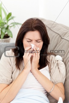 Portrait of a sick woman blowing her nose on the sofa