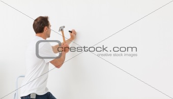 Rear view of a man hammering against a white wall