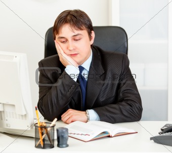 Bored modern businessman sitting at desk in  office
