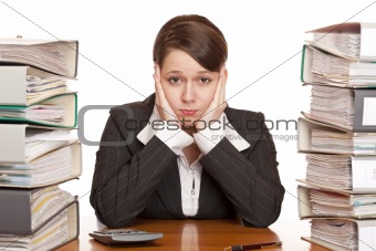 Frustrated overworked business woman in office between folder stack