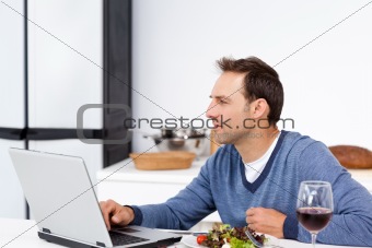 Concentrated man looking at his laptop while eating a salad