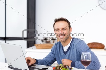 Happy man looking at his laptop while eating a salad 
