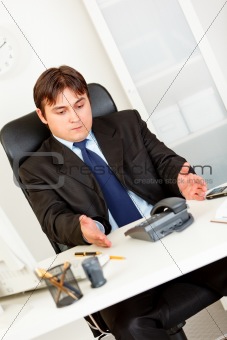 Displeased businessman sitting at office desk and waiting important phone call
