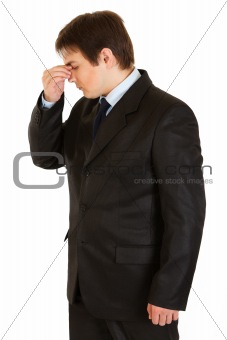 Stressed young  businessman holding fingers at noseband
