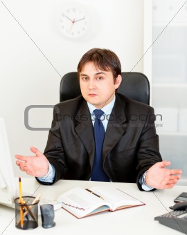 Confused modern businessman sitting at office desk
