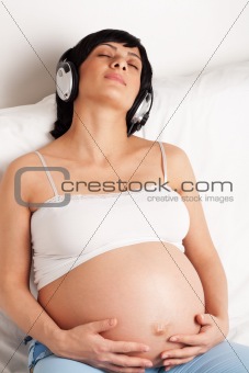 Pregnant woman sitting on sofa and listening music