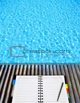 open notepad place on wood floor beside the blue swimming pool
