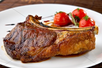 Grilled meat ribs on white plate with tomatoes