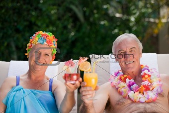 Mature couple drinking a cocktail  beside the swimming pool