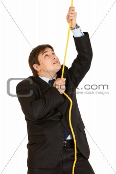 Stubborn young businessman climbing up on rope

