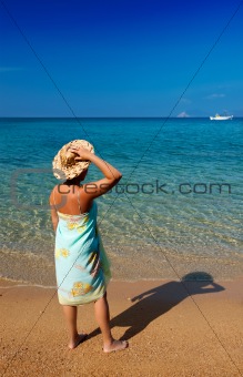 Young woman in pareo and straw hat looking into the deep blue se
