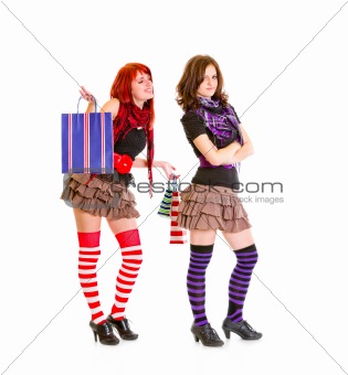Happy young girl with shopping bags standing behind her dissatisfied girlfriend
