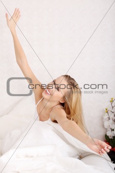Happy young woman stretching in bed