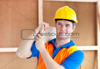 Assertive young male worker with a yellow helmet carrying a wood