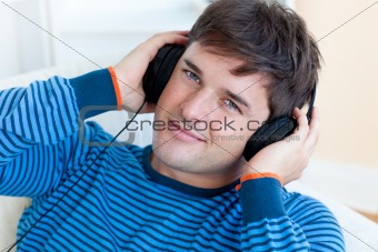 cheerful man listening music with headphones on lying in the liv
