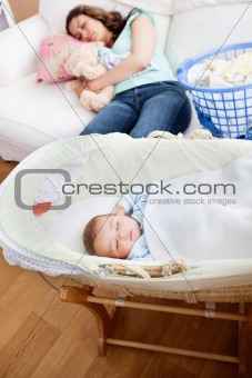 Young mother sleeping on the sofa while her baby is sleeping in 