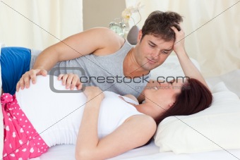 Delighted caucasian pregnant woman lying on bed with her husband