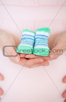 Close-up of a caucasian pregnant woman holding baby shoes and of