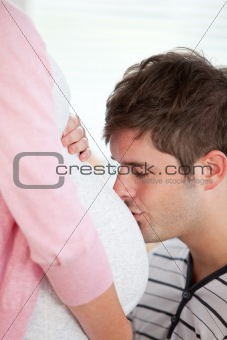 Portrait of an affectionate man kissing the belly of his pregnant