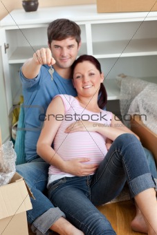 Happy couple expecting a baby sitting on the floor and holding t