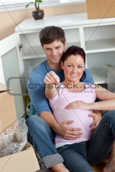 Delighted couple expecting a baby sitting on the floor and holdi
